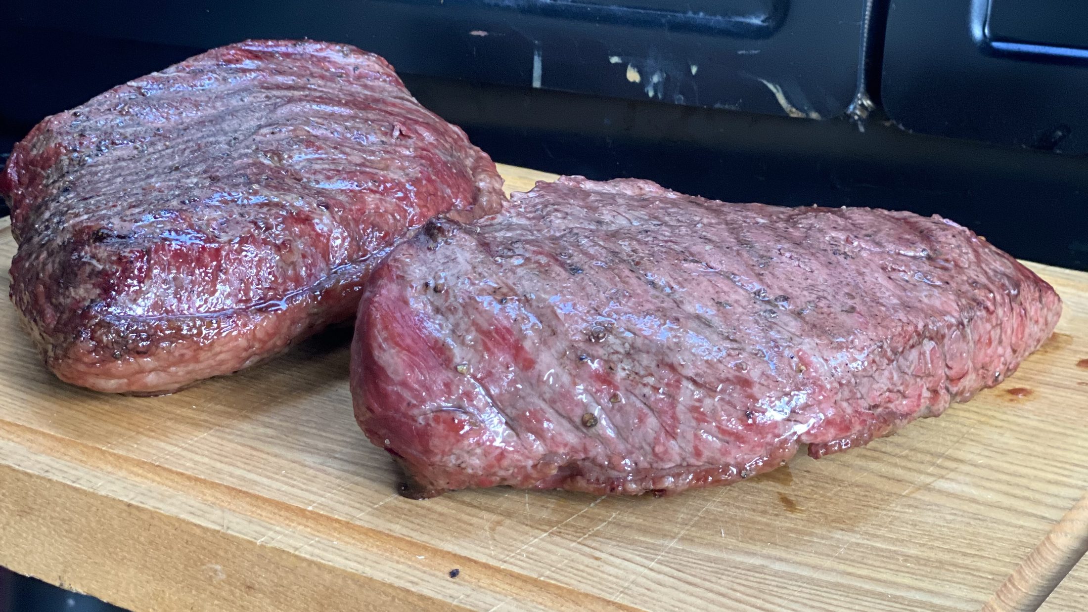 Twee gegrilde steaks op een houten snijplank voor de zwarte houtgestookte smoker